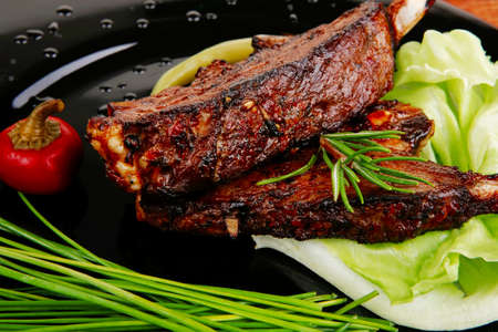 image of served meat: spiced barbecued ribs on black plate with peppers chives and capersの写真素材