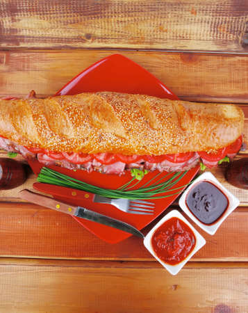 fresh white baguette with chicken smoked sausage on red ceramic plate over wooden tableの写真素材