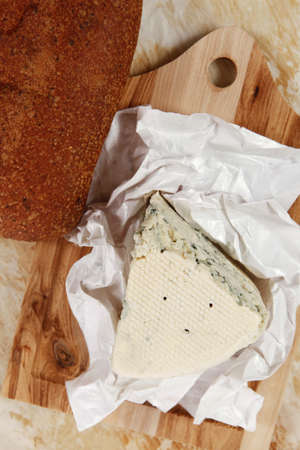 aged italian deli fresh blue stilton cheese and rye ciabatta served on wooden cutting plate on used baking paper as backgroundの写真素材