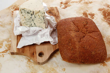 aged italian deli fresh blue stilton cheese and rye ciabatta served on wooden cutting plate on used baking paper as backgroundの写真素材