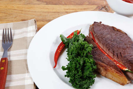 grilled beef steak fillet meat with red hot pepper and  raw kale leaf with ketchup sauce served on white plate over wood tableの写真素材