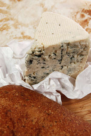 aged italian deli fresh blue stilton cheese and rye ciabatta served on wooden cutting plate on used baking paper as backgroundの写真素材