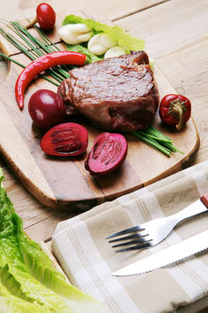 bbq : beef (pork) steak garnished with green staff and red chili hot pepper on wooden table with cutleryの写真素材