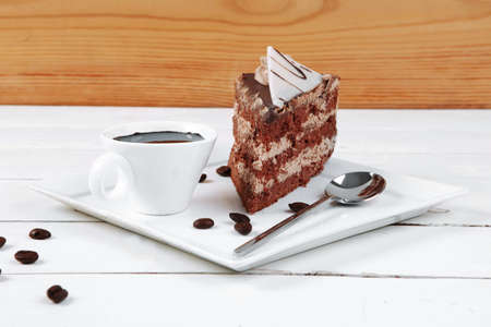 breakfast hot coffee mug and cream chocolate layer cake decorated with white chocolate slice and cream flower on white plate over woodの写真素材