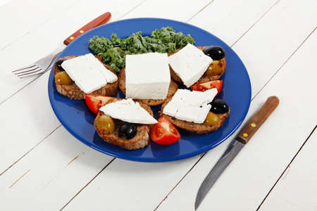 white feta greek cheese sandwich rye bread on blue plate with black spain olives tomatoes and cutlery over retro wooden tableの写真素材