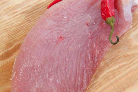 raw fresh turkey meat steak fillet cuts on wooden board with red hot chili pepper isolated over...