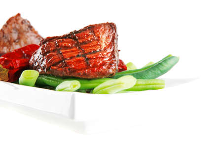 served grilled beef veal fillet entrecote on a white plate with peppers and green peas on long plate isolated on white backgroundの写真素材