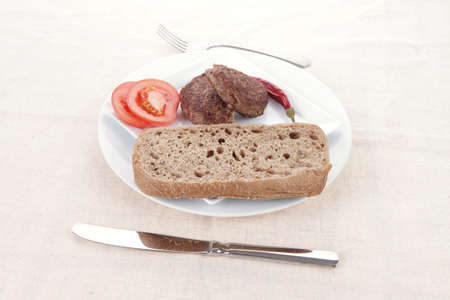 ripe beef meat hamburger on white plate with rye bun on white plate with cutlery on tableclothの写真素材