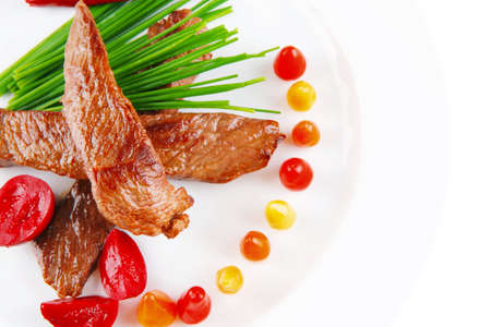 hot fresh grilled red beef meat fillet with vegetables green chives and peppers on china plate isolated over white backgroundの写真素材