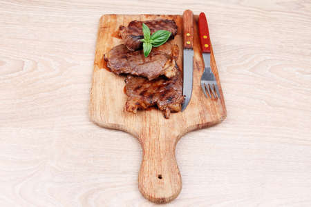 grilled beef on wooden plate with cutlery over tableの写真素材