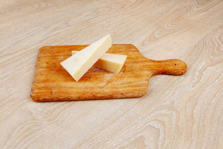 two fresh triangle french delicacy parmesan cheese pieces on wooden cut board over tableの写真素材