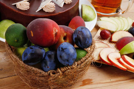 whole big chocolate cream brownie cake topped with white chocolate and cream flowers with hot tea cup decorated with fruits apple plum and grape on plate on wooden tableの写真素材