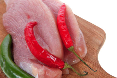 fresh raw turkey meat pieces on wooden cutting plate with red and green hot chili pepper isolated over white backgroundの写真素材