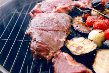 fresh raw beef fillet steak red meat with tomatoes and eggplant on skewers on big round barbecue brazier grid full with ready charcoalの写真素材