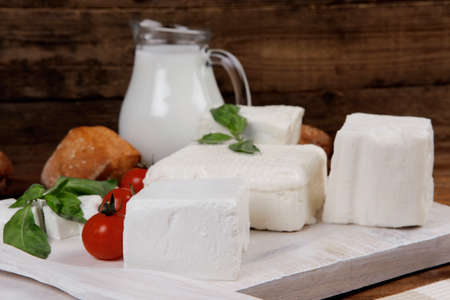dairy food fresh white greek goat sheep feta cheese on plate with milk in pitcher cherry tomatoes french bun over dark wooden tableの写真素材