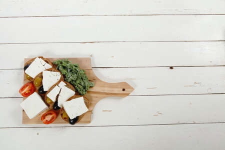 fresh greek feta cheese sandwich on wooden plate with hot green olives and black, goat cube, tomatoes kale over tableの写真素材