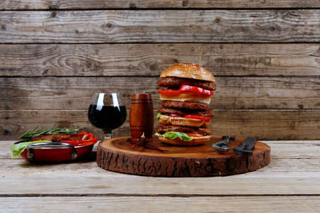 fresh grilled beef huge hamburger served on wood plate with red wine glass chili pepper rosemary green salad leaf and forged vintage antique cutlery over wooden table empty space for textの写真素材