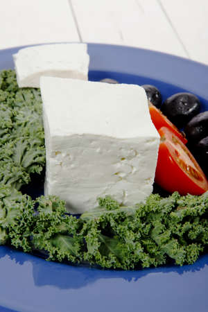 white goat feta cheese with black olives and tomatoes on blue plate over wooden tableの写真素材