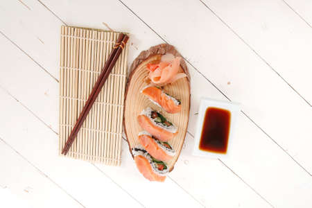 onigiri sushi salmon rolls with soy sauce on wooden plate and bamboo mat on white table with sticksの写真素材