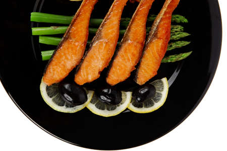 grilled salmon slices with asparagus lemon and olives on black plate isolated over white backgroundの写真素材