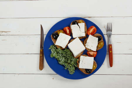 white feta greek cheese sandwich rye bread on blue plate with black spain olives tomatoes and cutlery over retro wooden tableの写真素材