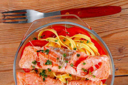 fresh fried natural pink salmon on italian traditional tagliatelles backed with tomato and vegetables served over wooden table with cutleryの写真素材