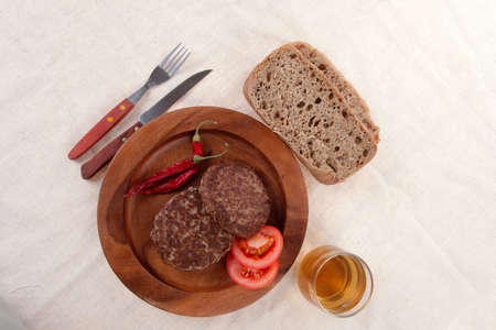 fresh beef meat hamburger on wooden plate with cutlery and rye bread bun on tablecloth with whiskey shotの写真素材