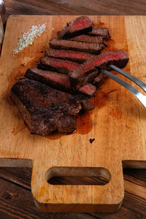 grilled beef fillet steak on fork over wooden board served with different kind of dry spices salt crushed black pepper hot baked sweet paprika red hot chili on dark tableの写真素材