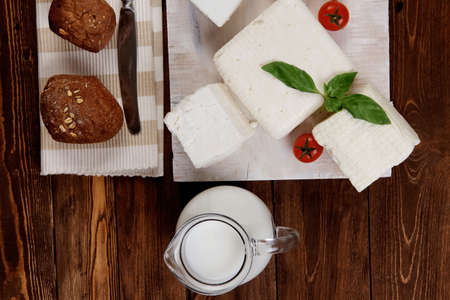 dairy food fresh white greek goat sheep feta cheese on plate with milk in pitcher cherry tomatoes french bun over dark wooden tableの写真素材