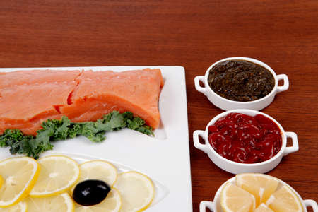 healthy food fresh raw red fish with kale lemon antipesto ketchup sauce on white plate over wooden tableの写真素材