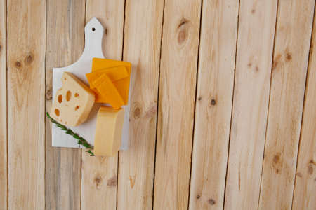various types of fresh raw aged delicatessen cheese on white plate over light wooden table cheddar edam swissの写真素材