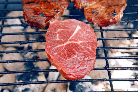 fresh raw beef fillet steak red meat on big round barbecue brazier black grid full burned charcoalの写真素材