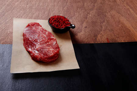 fresh raw beef rib eye steak on black walnut wooden table with red hot pepper spice in saucerの写真素材