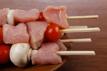 fresh raw meat fillet shish kebab turkey pork pink on skewers tomatoes mushrooms on wooden dish on big wood tableの写真素材
