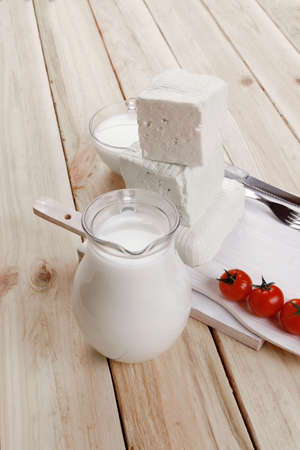 healthy dairy food fresh white greek goat sheep feta cheese on plate with milk in glass and full jug cherry tomatoes french bun over light wooden table with cutleryの写真素材