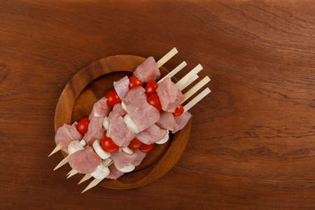 fresh raw meat fillet shish kebab turkey pork pink on skewers tomatoes mushrooms on wooden dish on big wood tableの写真素材