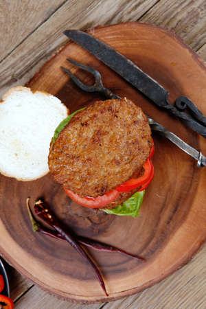 fresh grilled beef huge hamburger served on wood plate with red wine glass chili pepper rosemary green salad leaf and forged vintage antique cutlery over wooden table empty space for textの写真素材
