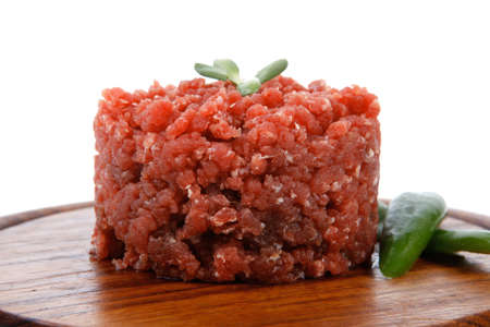 very big raw hamburger cutlet with sprouts and chilli pepper on wooden plate isolated over white backgroundの写真素材