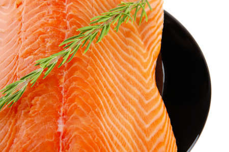 raw fresh uncooked salmon red fish fillet on black plate with rosemary twig isolated over white backgroundの写真素材