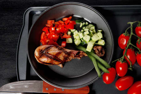 fresh hot grilled turkey drumstick leg with vegetables on black metal plate over wooden tableの写真素材