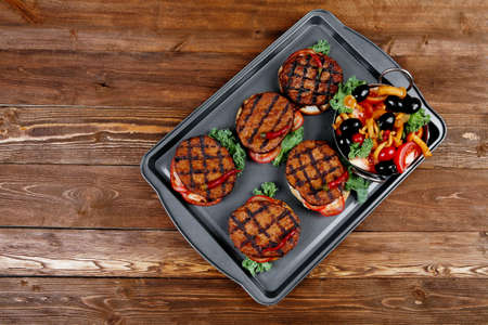 fresh red meat beef hamburger served on black tray with vegetables olives hot chili pepper tomatoes mushrooms over wooden table with empty space for text on backgroundの写真素材