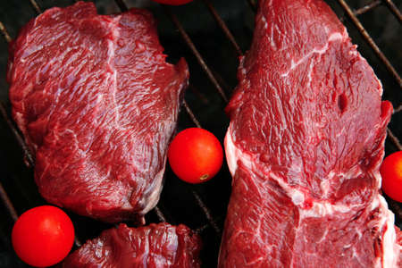 fresh raw beef steak with cherry tomatoes on black bbq grill ready to prepareの写真素材