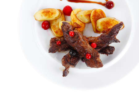 grilled beef meat with berries fried potatoes and cherry under sweet honey sauce on white plate isolated over white backgroundの写真素材