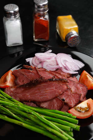 business lunch fresh roast beef meat slices on black plate wotj cutlery asparagus boiled broccoli rye bun on wooden tableの写真素材
