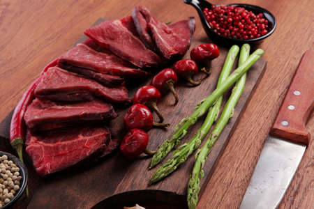 fresh beef meat asparagus greenery spices cutlery wooden table pepper crushed hot chili vegetables bowl served garlic cutting boardの写真素材