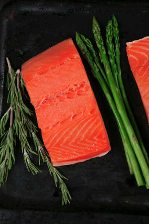 two piece of fresh raw pink salmon on black tray with rosemary and asparagus dry spices healthy food diet cooking conceptの写真素材
