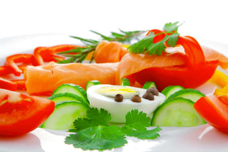 smoked salmon slices with vegetabls over white plateの写真素材