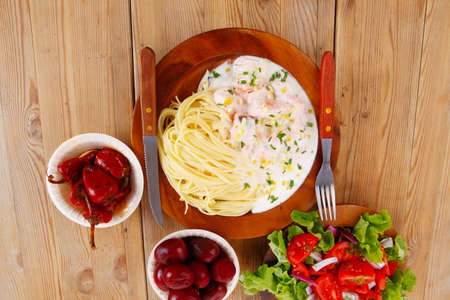 mediterranean cuisine: fresh rose wild salmon baked in cream cheese sauce with italian pasta and red hot pepper on wooden dish over table with vegetable saladの写真素材