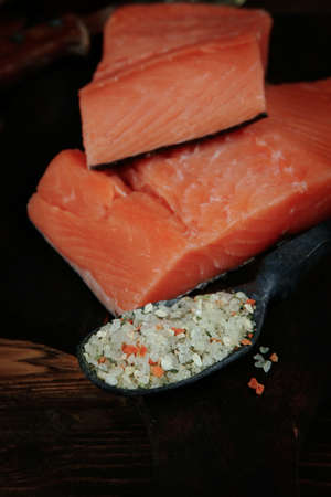 fresh raw salmon fillet served with lemon and white wine in wineglass, bottle, on dark plate over vintage wood table with handmade cutlery knife and spice on spoonの写真素材