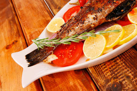 healthy lunch : whole fried sea sunfish on wooden table with lemons peppers and tomatoes and...